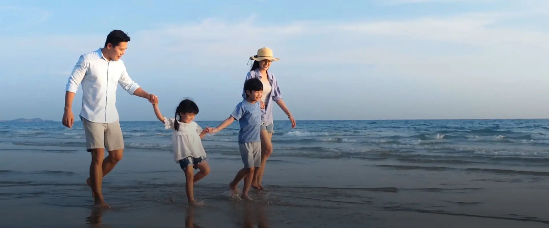 Asian family of 4 walking on the beach, holding hands 